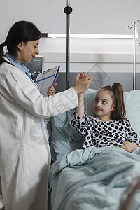 儿科专家与生病的小孩坐在病人床上做高五下手势图片