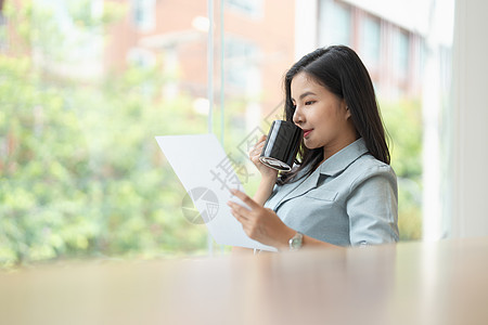 穿着优雅西装的美丽亚洲女商务人士坐在办公桌前 手里拿着一杯咖啡 女企业家 企业主成功商业女孩经理休息人士职场办公室成人电话图片