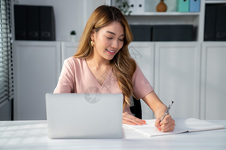 一位年轻的亚洲妇女坐在办公室的办公桌前成人管理人员微笑女士员工经理桌子会计办公房工人图片