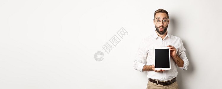 戴眼镜的惊讶男子 展示数字平板屏幕 看着惊异的人 站在白色背景上广告人士雇主商业员工技术男人药片衬衫购物图片