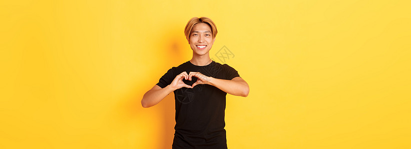 美丽英俊金发亚洲男子的肖像 展示了心动和微笑 站在黄色背景上理发快乐广告工作室男性职业员工男朋友发型购物图片