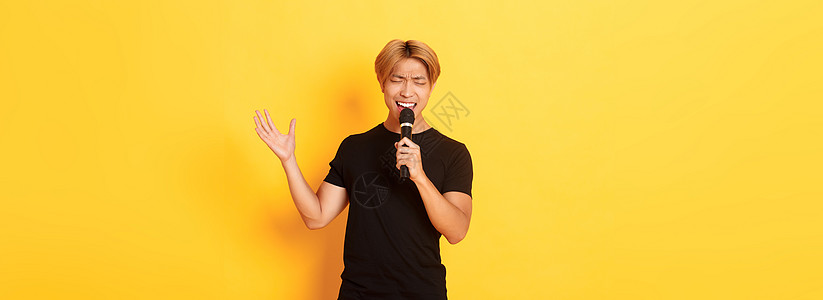 英俊的男性歌手 韩国人唱着歌 在卡拉OK用麦克风 用激情和热情地在黄色背景上站立潮人工作室理发职业发型学生广告促销购物头发图片