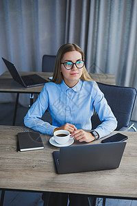一位身穿衬衫 戴着眼镜的漂亮女商务人士坐在办公室的桌旁 手里拿着一台笔记本电脑 在现代办公室工作场所戴眼镜的女经理 在电脑前的工图片