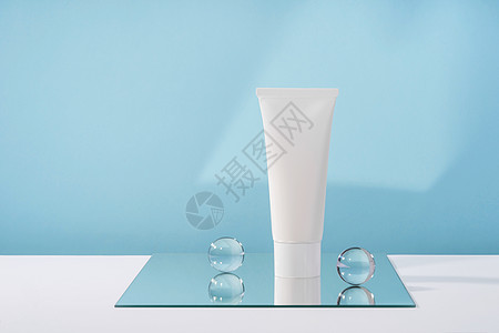 蓝色背景的无品牌化妆品奶油白色塑料管样机 配有时尚的道具 镜子和玻璃球 美体保健美容产品包装图片