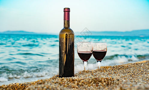 一瓶酒和杯子 在海边的海滩上 面对松绿海浪图片