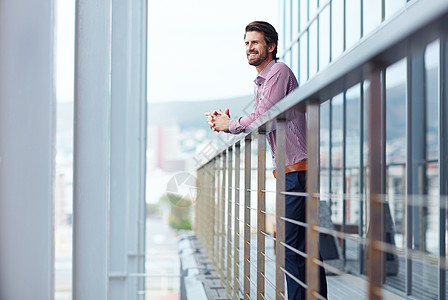 在阳台上小憩 一个快乐的年轻商务人士站在办公楼的阳台上图片