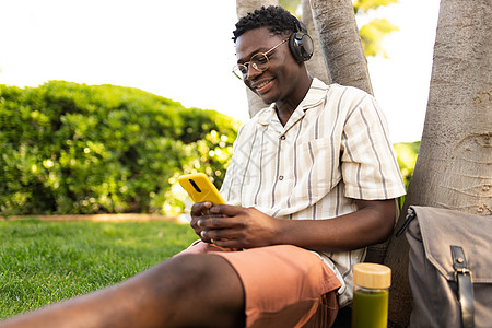 非洲男子在户外休闲 用电话和耳机听音乐 黑人大学生在校内学习 复制空间 校外活动图片