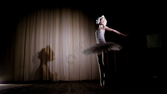 在聚光灯下 在旧剧院大厅的舞台上 穿着白天鹅和足尖鞋的年轻芭蕾舞演员 优雅地跳着某种芭蕾动作 天鹅湖足尖舞成人爱好舞蹈工作室艺术图片