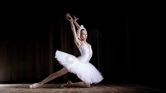 在聚光灯下 在旧剧院大厅的舞台上 穿着白天鹅和足尖鞋的年轻芭蕾舞演员 优雅地跳着某种芭蕾舞动作 部分是胸罩工作室女士女性训练商店图片