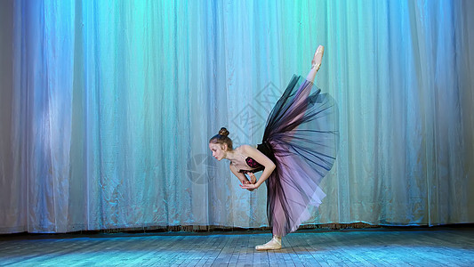 芭蕾排练 在旧剧院大厅的舞台上 身穿淡紫色黑色连衣裙和足尖鞋的年轻芭蕾舞演员 优雅地跳着某种芭蕾舞动作 在背后抬起腿图片
