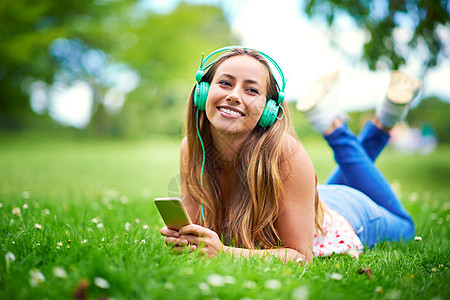 音乐和自然能让灵魂舒缓 一个年轻女人躺在公园的草地上听音乐图片