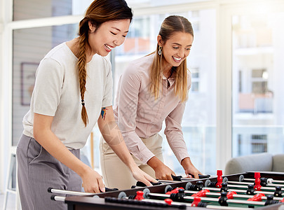 女商务人士踢桌上足球 大笑 在公司工作中享受办公室乐趣 不同的女同事在休息时一起参加友好的桌上足球比赛图片