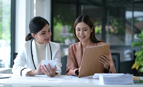 两位年轻的亚洲女商务人士讨论投资项目工作和规划战略 商界人士在办公室与笔记本电脑交谈微笑管理人员女性会议客户女士文档成功合作同事图片