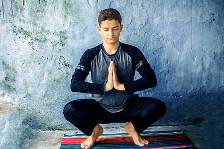 穿黑色衣着和做瑜伽的少年男孩 在多彩的传统垫子上做瑜伽 做著名的加兰姿势或马拉萨纳图片