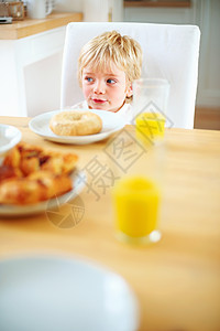 可爱的小男孩吃早餐 桌上放着甜甜圈和果汁 一个可爱的小男孩的画像 他在桌上吃着甜甜圈和果汁吃早餐图片