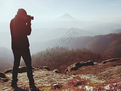 专业摄影师在岩石高峰用镜像照相机拍照 梦雾般的雾运动员背包男人相片薄雾晴天远足顶峰镜子天空图片