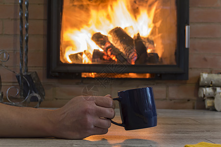 一个人的手拿着杯子 在壁炉附近喝热水和火 冬天在温室里保持温暖图片