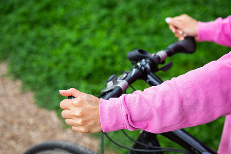一个穿着粉色运动衫的女孩抓着自行车的车把 在公园里骑自行车 户外休闲有益于健康图片
