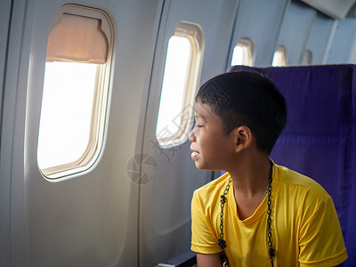 一个亚洲男孩坐着微笑 看着飞机窗外的风景航班飞行旅行办公室关爱假期运输儿子窗户座位图片