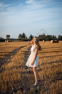 一名身着白裙子的金发女孩在收割黑麦田中行走的照片图片