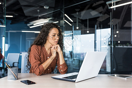 在现代产品开发公司工作的沉思而专注的女性程序员网络开发人员西班牙裔女性坐着思考使用笔记本电脑编写代码女士软件学习技术多样性程序思图片