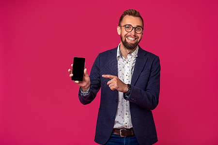 年轻快乐的律师或商务人士站在粉红背景上微笑 展示他的智能手机的黑屏幕 笑声掌声互联网就业人士工作时尚套装细胞喜悦夹克男性图片