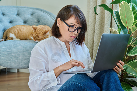 中年妇女使用笔记本电脑 睡猫躺在扶椅上图片