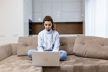 在家工作的年轻妇女 坐在沙发上 手持笔记本电脑 耳机和麦克风 检疫 远程工作 自由职业者电子邮件公寓家居房子休闲摄影女性学习商业图片