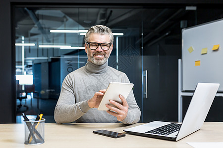 成功的程序员团队负责人的肖像 成熟的白发工程师在平板电脑上测试新应用程序 在现代办公大楼内工作的商务人士 微笑着看着相机图片