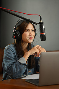 使用冷缩麦克风和膝上型电脑在小型家庭录音室录制播客的正面女性电台主持人图片
