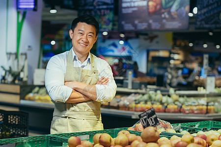 一个快乐英俊的亚洲推销员的画像 市场或杂货店的蔬菜和水果 卖方 一个围裙的男人看着镜头 微笑着农民小企业主蔬菜水果商图片