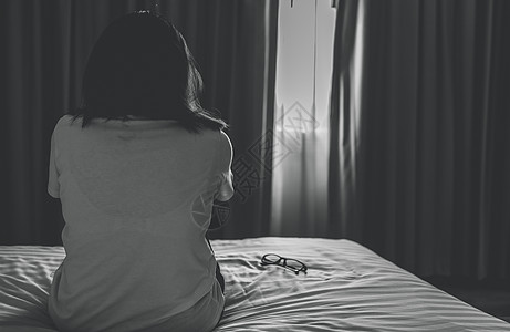 悲伤和沮丧的女人的后视图摘下眼镜 坐在酒店卧室的床上 悲伤的女人坐在黑暗的卧室里 有心理健康问题的女孩 不快乐的生活 世界精神卫图片