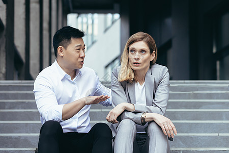 一名年轻女性和一名亚裔男性坐在办公中心前的台阶上 并争吵图片
