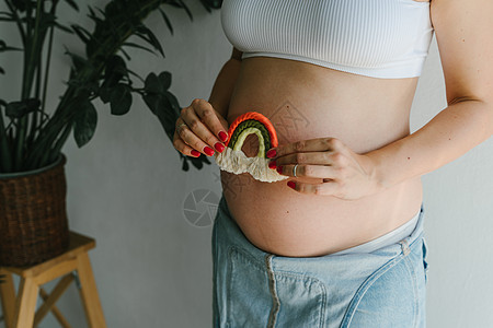 身穿牛仔裤的怀孕女孩手里握着彩虹来装饰一个儿童房间 她拿着彩虹孩子女人父母肚子生活腹部妈妈手工身体母性图片