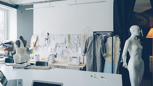 轻便的服装设计工作室 配有大型裁缝桌 人体模型 墙上钉着的大量草图 缝纫机和挂在栏杆上的半成品服装图片