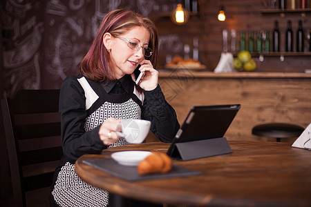 成功的成年女商务人士通过电话交谈 同时咖啡喝一杯咖啡 (b)图片