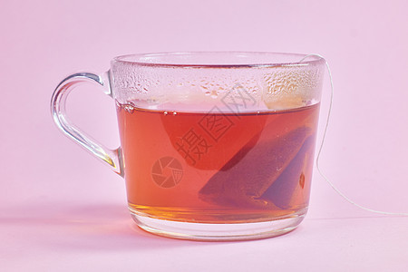 茶袋是用粉红背景的透明玻璃杯制成的图片
