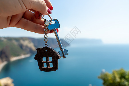 在大海的背景下 女性手中拿着房子形状的钥匙链钥匙 购买房屋 公寓 房地产 年轻家庭 抵押贷款 出租房屋的概念贷款动作安全玩具代理图片