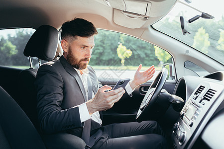 坐在汽车方向盘后面的男性商务人士 沮丧地无法理解转向和指示时髦的汽车 从电话中读取更多信息帮助压力保险旅行人士车辆愤怒车祸员工套图片