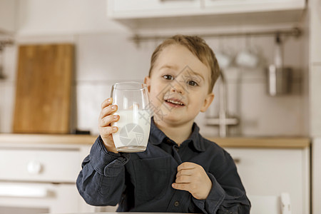 小男孩坐在厨房里喝牛奶 玻璃杯中的新鲜牛奶 乳制品健康饮料 医疗保健 钙源 乳糖 舒适而现代的内饰 穿着休闲服的学龄前儿童图片