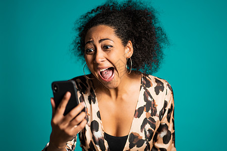 愤怒潮流的非洲女人在工作室尖叫着她的手机 带着蓝背景的压抑和压抑的女孩图片