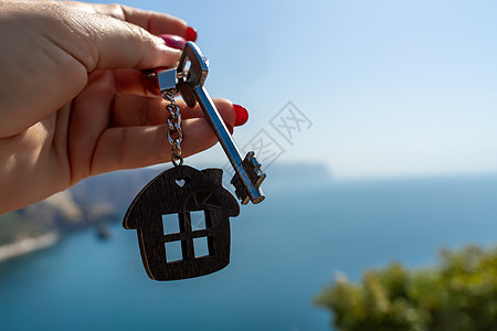 在大海的背景下 女性手中拿着房子形状的钥匙链钥匙 购买房屋 公寓 房地产 年轻家庭 抵押贷款 出租房屋的概念房间安全标签销售金属图片