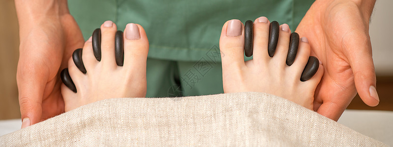 在温泉疗养所 女性按摩师手中的女脚趾之间用黑石头进行脚底按摩修脚岩石福利护理中心毛巾保健享受奢华皮肤图片