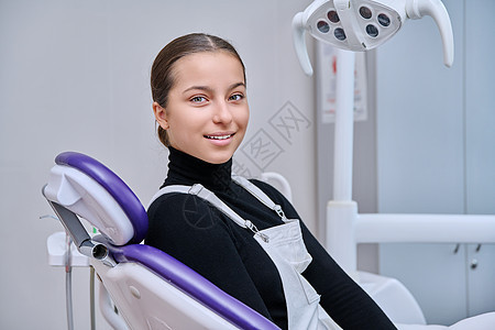 年轻笑笑的少女坐在牙科椅上看着镜头的肖像椅子成人医生药品保健幸福女性微笑办公室医院图片