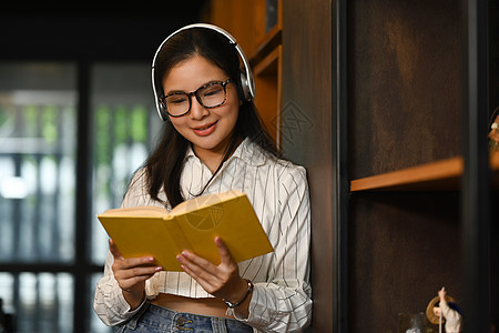 大学妇女佩戴耳机和图书馆阅读书的肖像 以及人 知识和教育概念 (续)图片