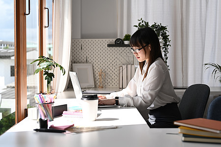 使用膝上型计算机 在明办公室从事营销项目工作;女雇员用笔记本电脑进行侧边视线图片