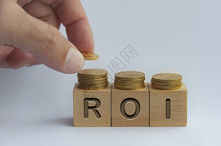 将硬币手放在木块上 用ROI文字刻在木块上-商业与投资概念图片