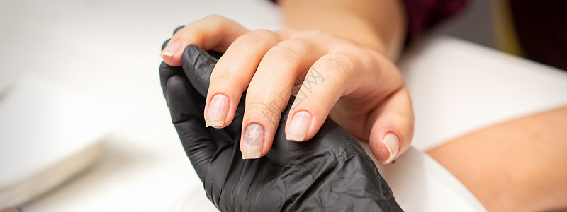 检查修剪过的指甲 在美甲沙龙里 戴着黑色手套的美甲大师的手在检查女性透明指甲治疗凝胶客厅化妆品温泉夫妻抛光女士客户程序图片