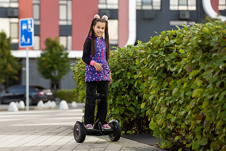 快乐的小姑娘站在户外的电动摩托车上孩子喜悦陀螺仪运输驾驶运动工具街道滚动乐趣图片