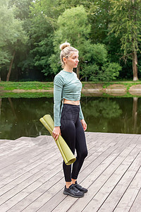 一个穿着绿色上衣和深色紧身裤的漂亮女人 站在夏天 带着绿色的运动垫图片